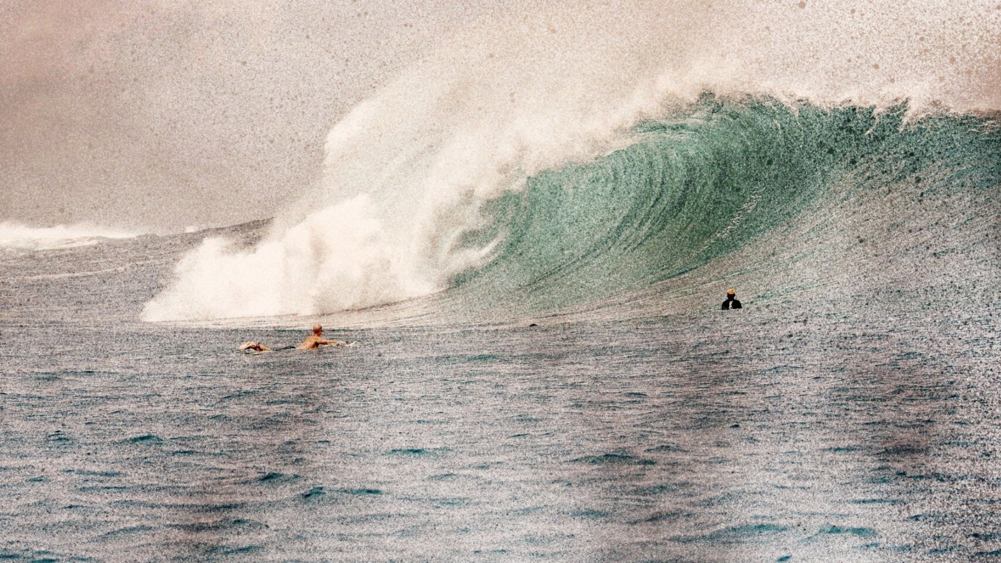 Surfer paddling toward a massive breaking wave